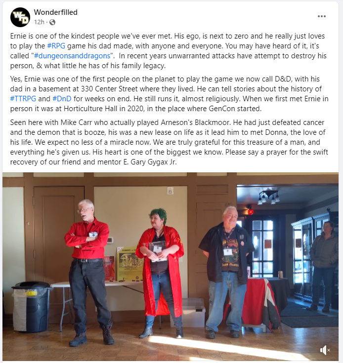 A screenshot of a Facebook post by Wonderfilled: Ernie is one of the kindest people we've ever met. His ego, is next to zero and he really just loves to play the #RPG game his dad made, with anyone and everyone. You may have heard of it, it's called #dungeonsanddragons.  In recent years unwarranted attacks have attempt to destroy his person, & what little he has of his family legacy.  Yes, Ernie was one of the first people on the planet to play the game we now call D&D, with his dad in a basement at 330 Center Street where they lived. He can tell stories about the history of #TTRPG and #DnD for weeks on end. He still runs it, almost religiously. When we first met Ernie in person it was at Horticulture Hall in 2020, in the place where GenCon started.  Seen here with Mike Carr who actually played Arneson's Blackmoor. He had just defeated cancer and the demon that is booze, his was a new lease on life as it lead him to met Donna, the love of his life. We expect no less of a miracle now. We are truly grateful for this treasure of a man, and everything he's given us. His heart is one of the biggest we know. Please say a prayer for the swift recovery of our friend and mentor E. Gary Gygax Jr.